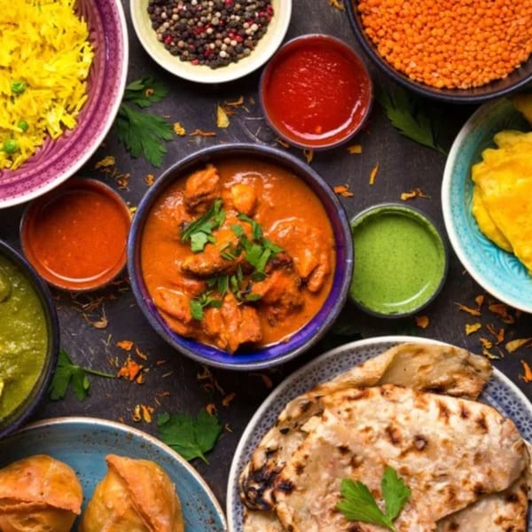 Overhead view of various Indian dishes including chicken curry, rice, naan, samosas, and sauces.