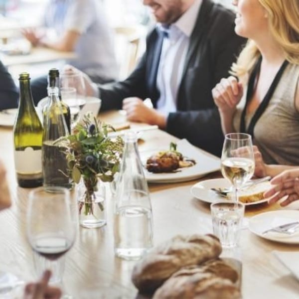 People dining at a restaurant table with wine, bread, and a main course.