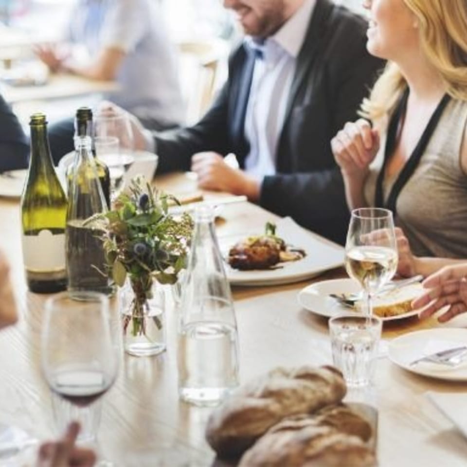 People dining at a restaurant table with wine, bread, and a main course.